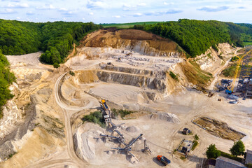 Open pit mining of construction sand stone materials with excavators and dump trucks at conveyor belt.