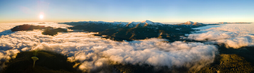 Aerial view of vibrant sunrise over white dense fog with distant dark Carpathian mountains on horizon.