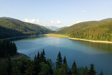 Fototapeta na wymiar Aerial view of big lake with clear blue water between high mountain hills covered with dense evergreen forest.