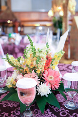 Table arrangement in a wedding party with flower bouquet and glasses of water on tablecloth with bokeh background. Selective focus on flower. No people.