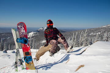 A man in snowboarding gear on the top of a mountain. Young man standing with a snowboard on the top...