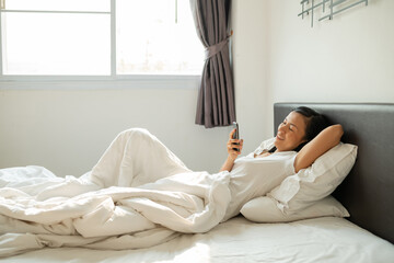 Asian woman with attractive smile use tablet smartphone on white bed, Portrait young beauty relax in bedroom. Technology people connection digital online marketing e-commerce concept