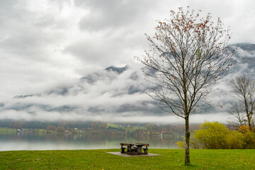 Fototapeta na wymiar Moody autumn landscape with bare tree and lonely bench on mountain lake shore.