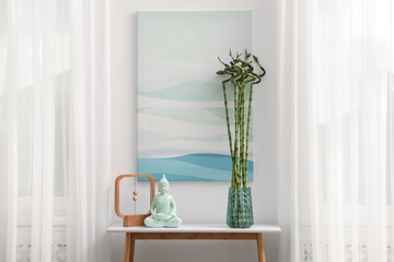 Console table with bamboo and Buddha statue near light wall indoors. Interior design