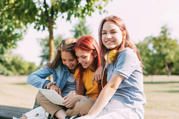 Attractive teenage girls are sitting on a park bench, discussing and smiling. Girlfriends are chatting in the park