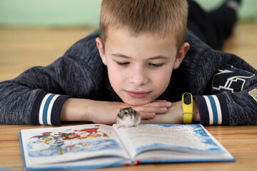 Close up portrait of smiling little boy reading book with small pet hamsters. Concept of studying with good mood.