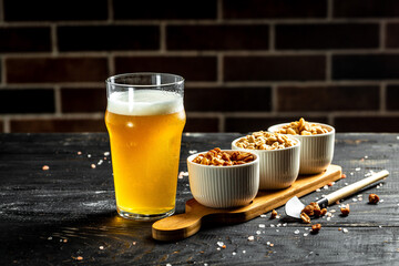 Glass with beer and set of various kind snacks salted nuts, stockfish on dark brown wooden background with copy space. Snacks for beer - obrazy, fototapety, plakaty