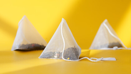 White pyramid tea bags with black and green tea flavored with fruits and berries lie in the sun on a yellow background. Imitation of ancient Egyptian pyramids and sand. Shallow depth of field