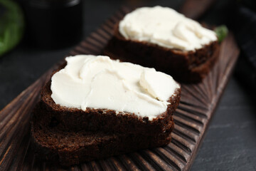 Bread with cream cheese on wooden board, closeup