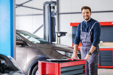 Mechanic pushing box with tools and preparing to fix a problem with car while walking in car salon.