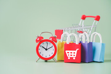 red clock with multi color shopping bags and blurred shopping cart  on green background, sales...