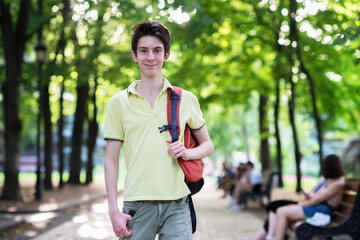 Young handsome 15 years old teen boy wearing yellow t-shirt with backpack looking at camera and happy smiling, summer park outdoor