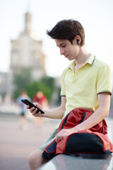 Young boy using smartphone over summer city outdoor. 15 years old teenager talking and sends messages by mobile phone, urban youth lifestyle