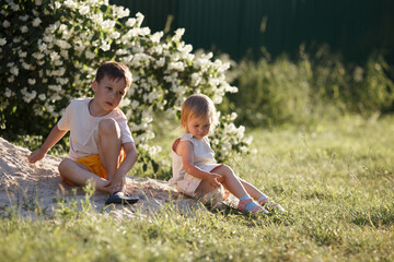 the older brother and his younger sister throw sand on the grass