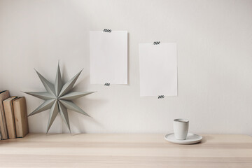 Blank greeting cards taped on white living room wall. Stationery mockup scene with grey folded paper star, cup of coffee and books on wooden table backgroum. Christmas decoration, winter composition. - Powered by Adobe
