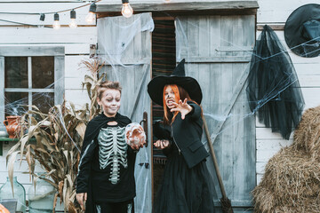 children a boy in a skeleton costume and a teenage girl in a witch costume having fun at a Halloween party on the decorated porch suburban house