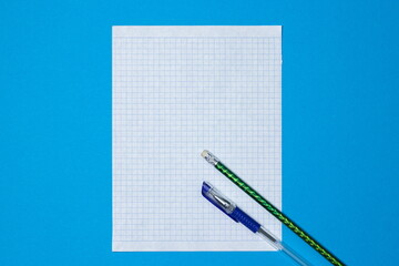 Blank squared paper for copy space on a blue background. A sheet of paper with a pencil and a pen.