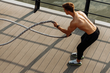 Naklejka premium Strong man training with fighting ropes, Sportsman doing battle rope training outdoors on the sea on the pier