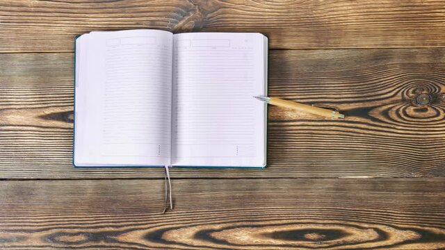 Stop motion animation of green school book notebook are moving with pen and opening on wooden background. Back to school, education concept. Top view.