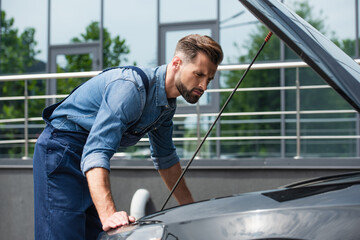 Pensive mechanic standing near car with open hood