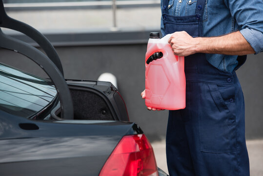 Cropped view of repairman holding canister of windshield washer fluid near auto