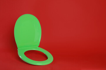 New green plastic toilet seat on red background, space for text