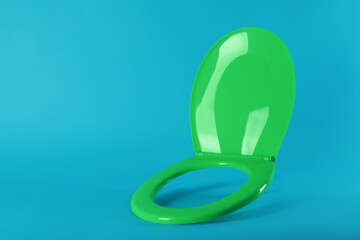 Obraz premium New green plastic toilet seat on light blue background, space for text