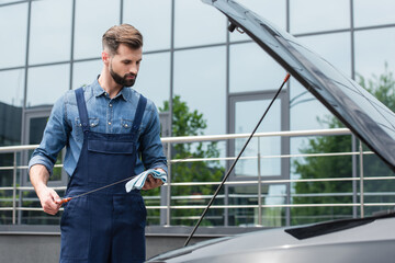 Mechanic with dipstick and rag looking at car outdoors