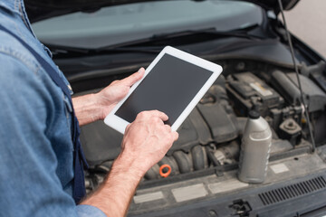 Cropped view of mechanic using digital tablet near blurred car