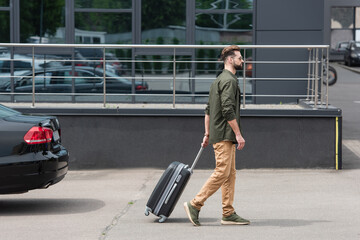 Fototapeta na wymiar Side view of man with suitcase walking near car outdoors