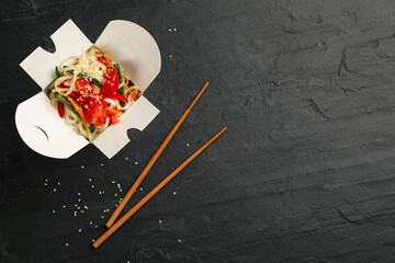 Box of vegetarian wok noodles with chopsticks on slate table, flat lay. Space for text