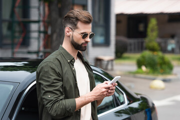 Man in sunglasses using mobile phone near car outdoors