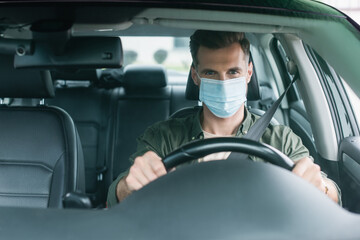 Driver in medical mask looking at camera in auto