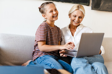 Fototapeta premium White mother and daughter smiling and using cellphone at home