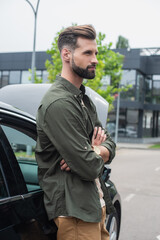 Side view of young man standing with crossed arms near car outdoors