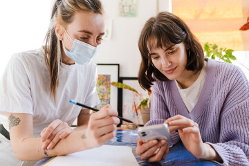 Young white women using cellphone while doing sketches in workshop
