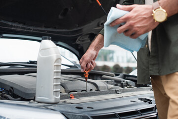 Cropped view of man checking oil of engine near bottle on car