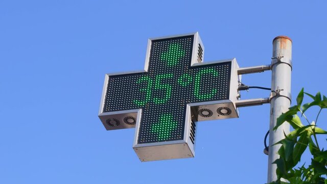 A cross-shaped pharmacy LED panel shows a temperature of 35 degrees celsius during a summer heat wave