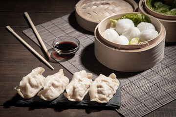 Dim sum in bamboo steamer and gyozas with soya sauce on dark background.