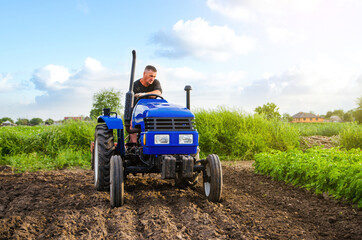 Obraz premium Farmer on a tractor works in the field. Seasonal worker. Recruiting workers with skills in driving agricultural machinery. Milling soil, loosening ground before cutting rows. Agriculture agribusiness