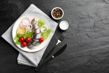 Fototapeta na wymiar Sliced salted herring fillet served with lettuce, onion rings, cherry tomatoes and lemon on black table, flat lay. Space for text