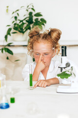 Little red-haired girl in white uniform conducting chemical experiments in a laboratory.Back to school concept.Young scientists.Natural sciences.Preschool and school education of children.