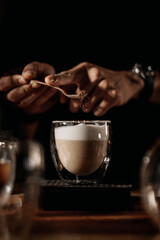 a hand of barista making and decoring a glass of coffee with milk foam
