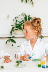 Obraz na płótnie Canvas Funny little red-haired girl in white uniform doing chemical experiments in a laboratory.Back to school concept.Young scientists.Natural sciences.Preschool and school education of children.