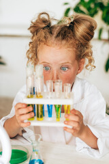 Surprised little red-haired girl in white uniform conducts chemical experiments in a laboratory.Back to school concept.Young scientists.Natural sciences.Preschool and school education of children.