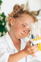 Little red-haired girl in white uniform conducts chemical experiments in a laboratory.Back to school concept.Young scientists.Natural sciences.Preschool and school education of children.