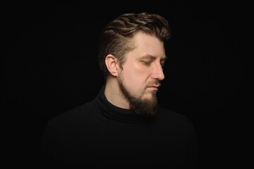 Thoughtful bearded man, half profile portrait, black background
