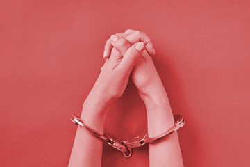Crossed hands in handcuffs on red background