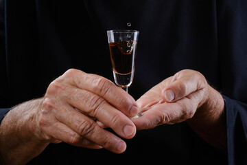 Close up of hands elderly woman holding shot glass or wineglass sedative drops or cognac . Selective focus on hands wrinkled skin.
