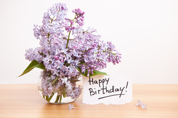 Happy birthday card with text and bouquet of lilac flowers	on the table